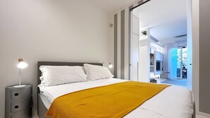A modern bedroom with a bed, a bedside table, and a view into an adjacent room. - Solemar Sicilia - White Loft (Palermo)