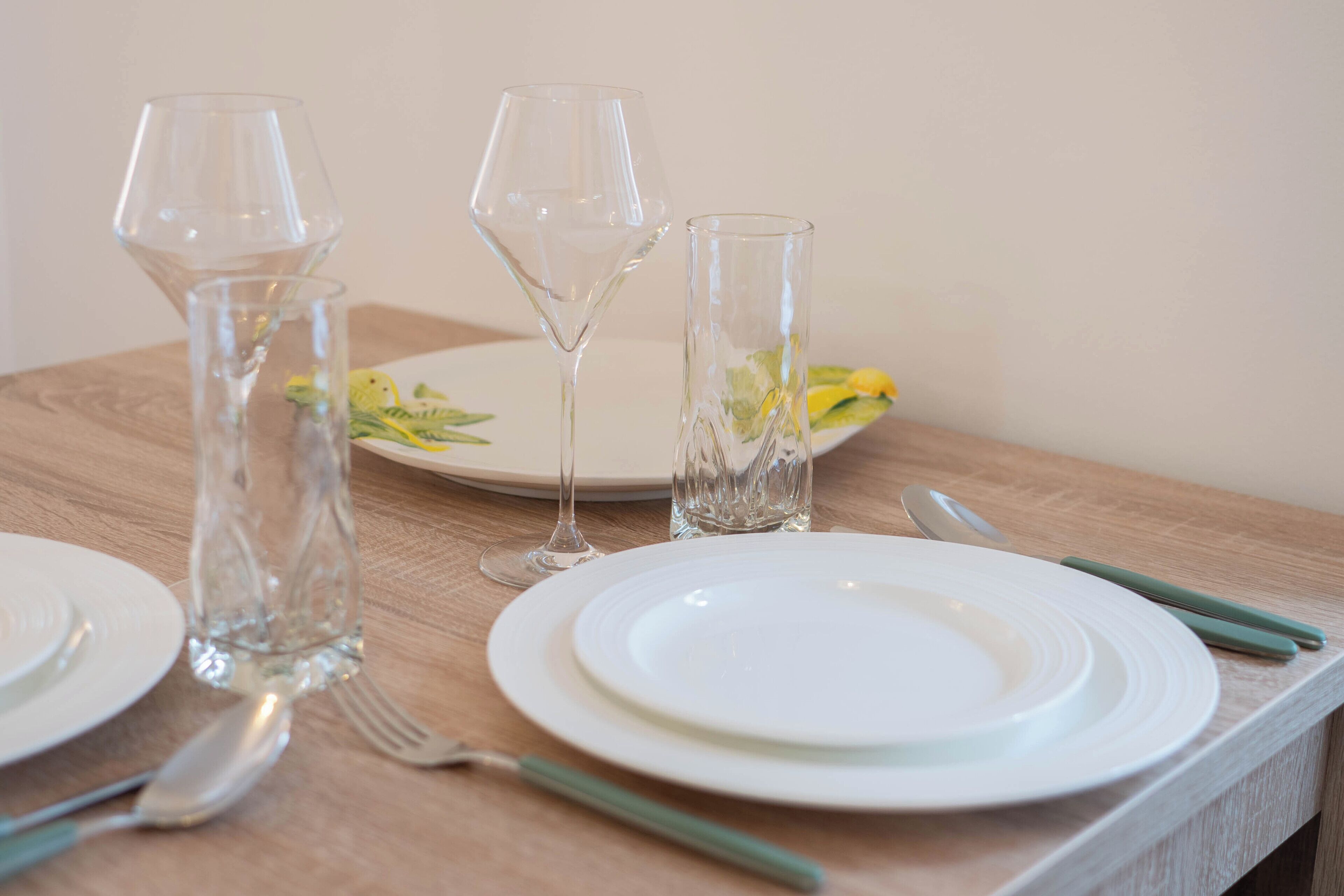 Une table à manger dressée avec de l’argenterie blanche, de la verrerie transparente et des couverts aux manches vertes.