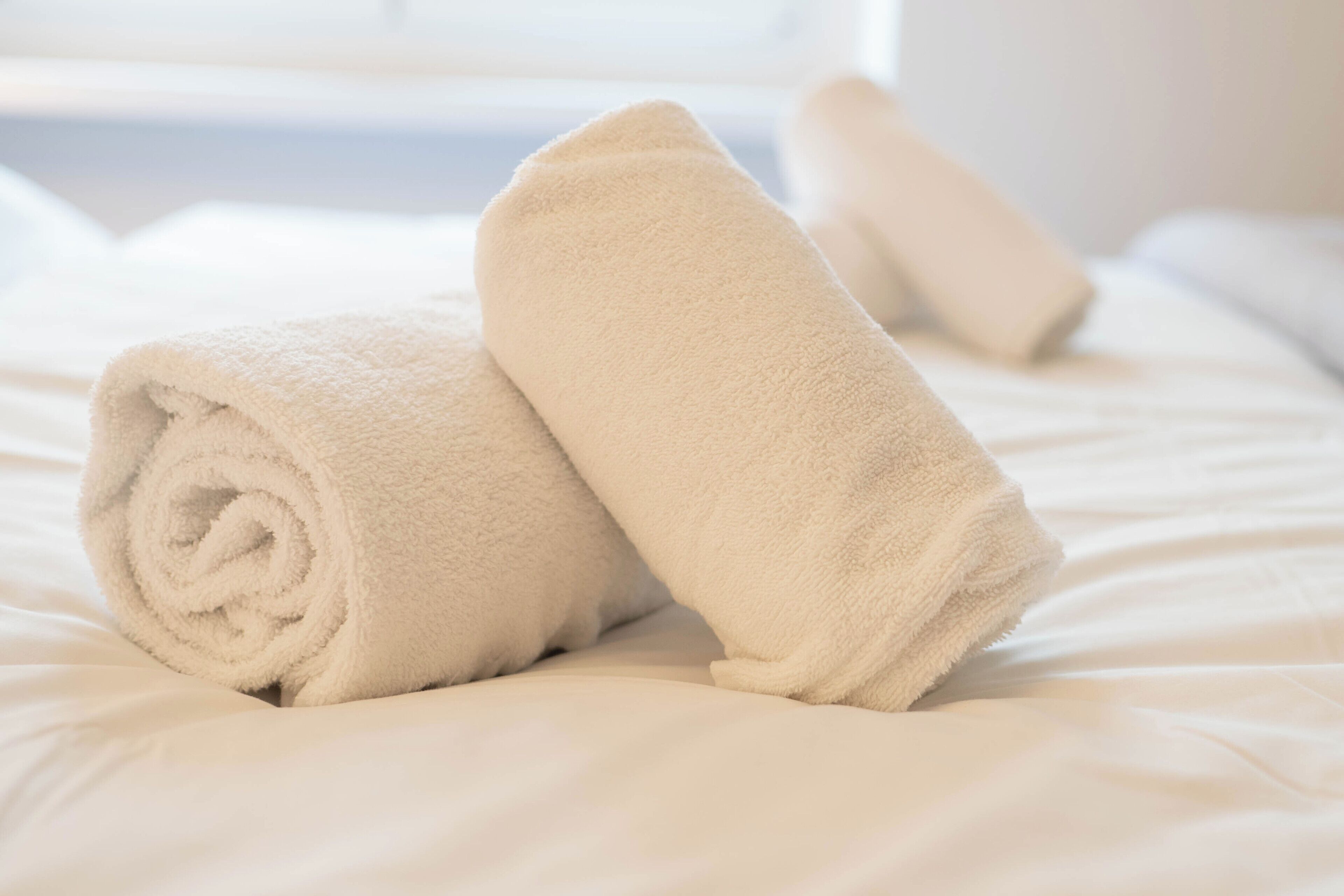 Un letto rifatto con lenzuola bianche e un asciugamano arrotolato.