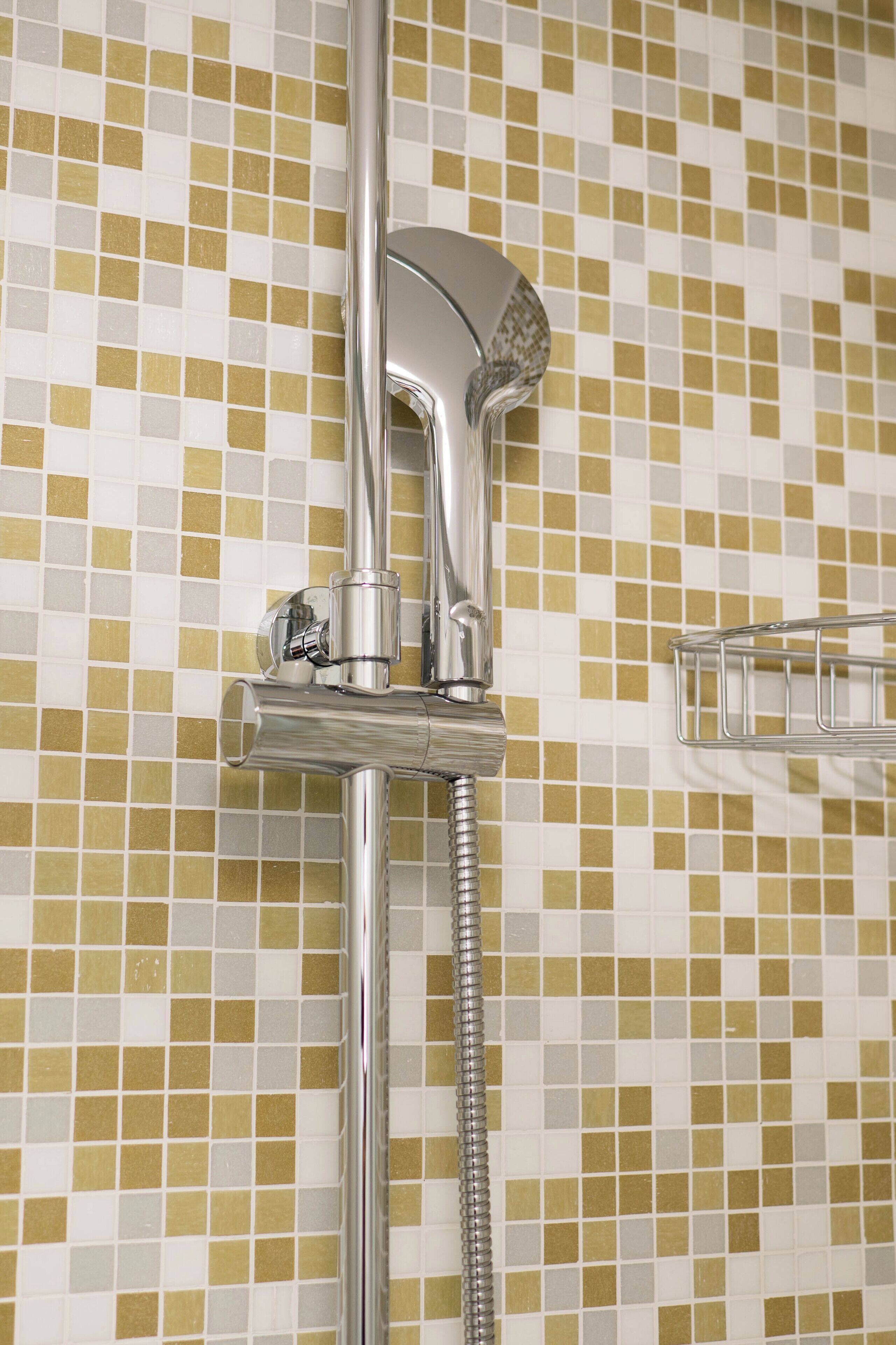 A chrome showerhead with a flexible hose against a mosaic tile wall.