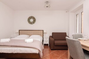 Un dormitorio con cama, una mesita de noche, un sofá marrón, una mesa de comedor con sillas y una araña.
