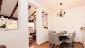 A dining area with a round table, grey chairs, and a chandelier. There is a window with white orchids and a view of a balcony. - Apartments Leonel Piran  (Piran)