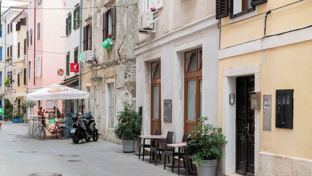 A street with outdoor seating, potted plants, and a scooter parked by the sidewalk. - Apartments Leonel Piran  (Piran)