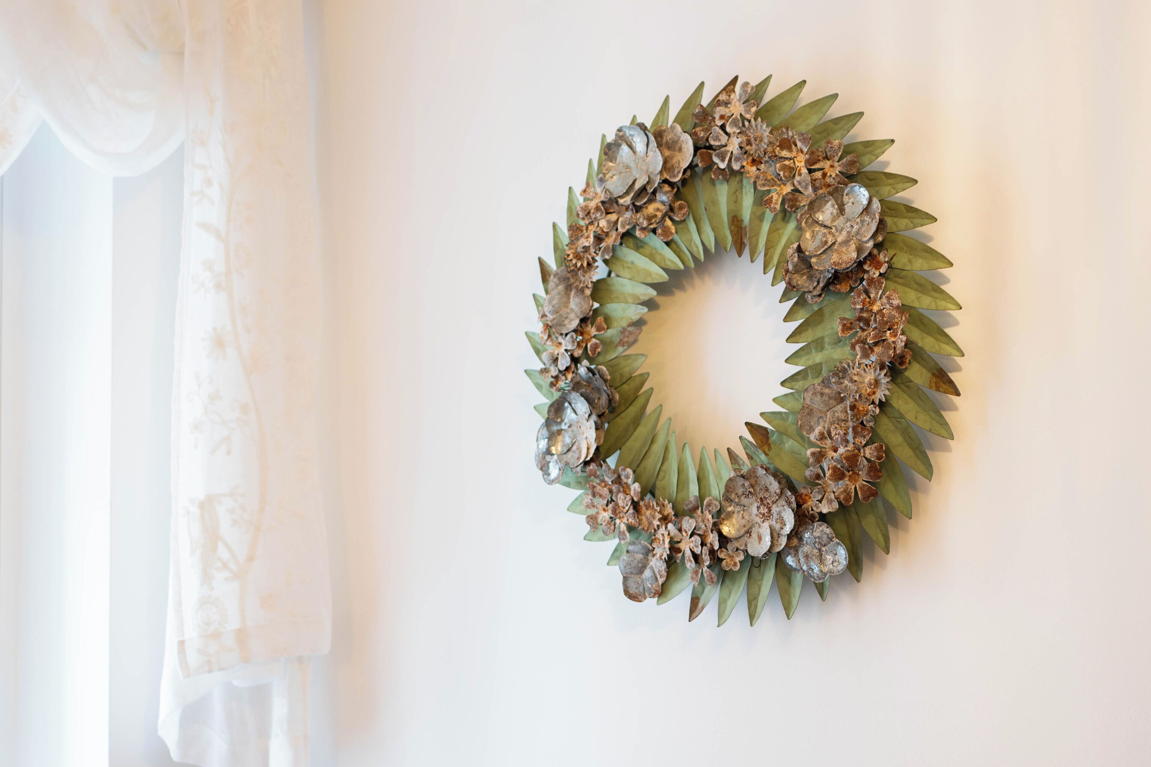 A wreath with green leaves and metallic flowers on a white wall.