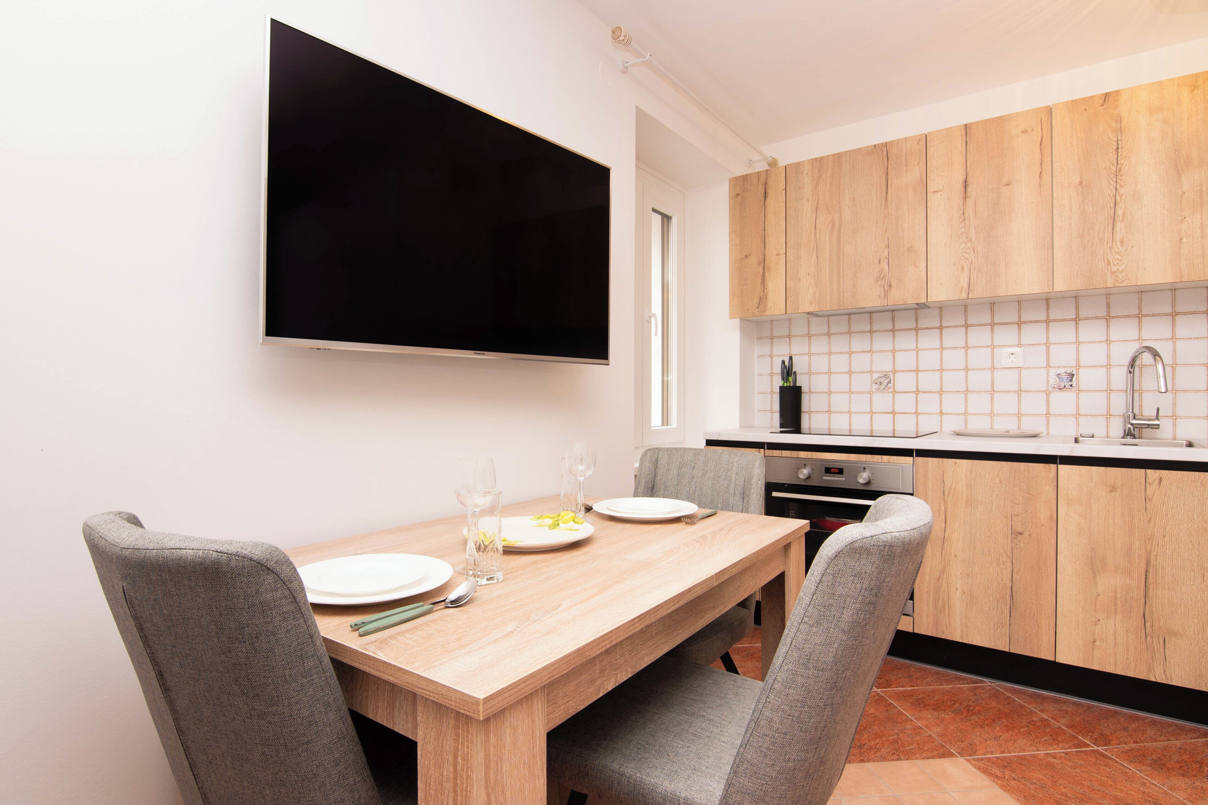 A modern kitchen with wooden cabinets, a tiled backsplash, and a dining area with a wooden table and grey chairs.