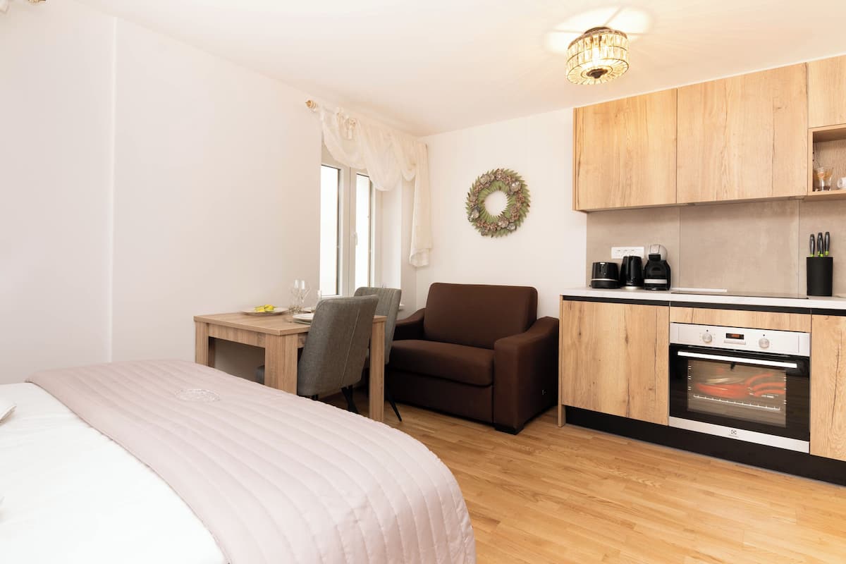 A compact room with a bed, a desk, a chair, a kitchenette, and a small dining area.