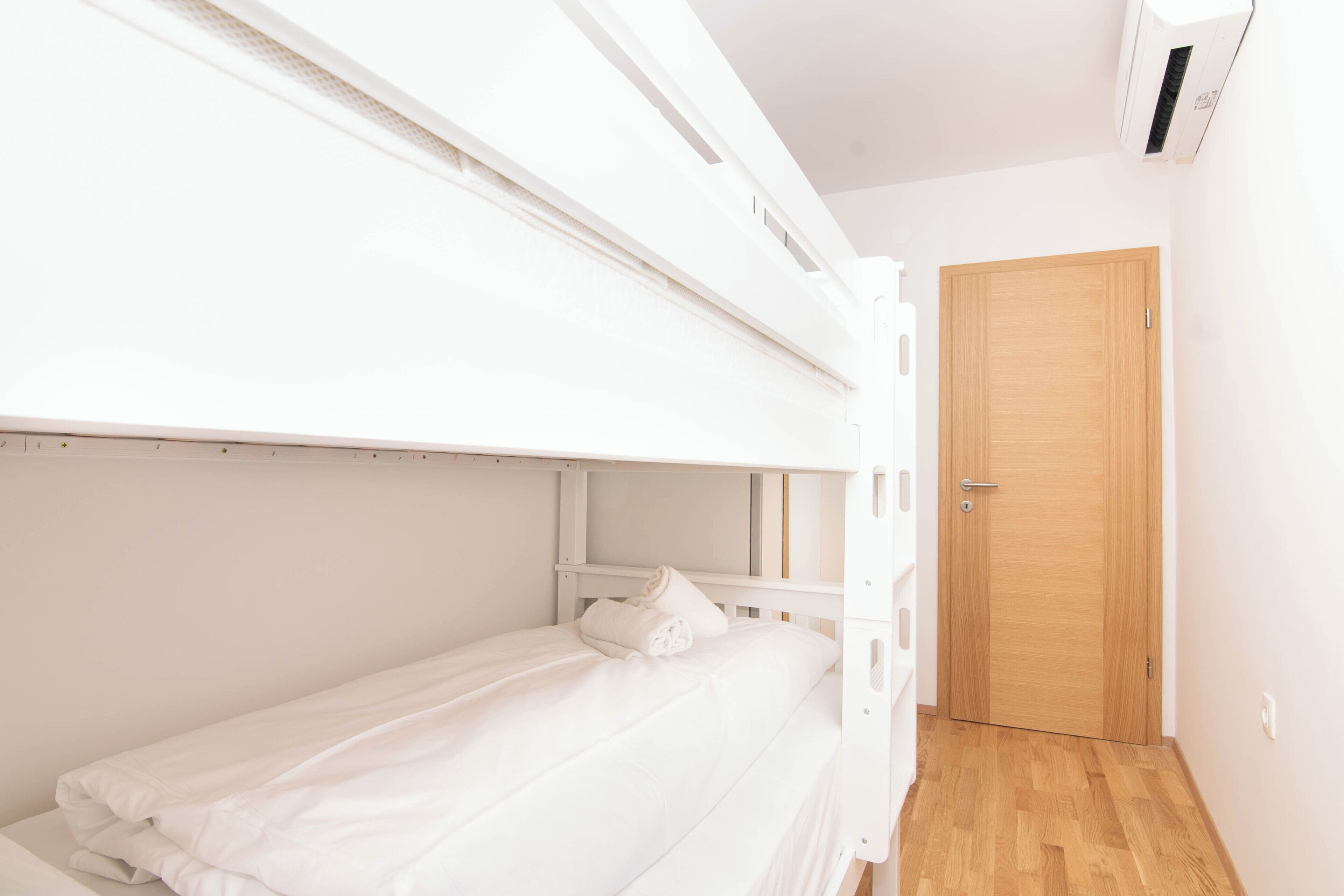 A bunk bed room with a wooden door and a white air conditioning unit.