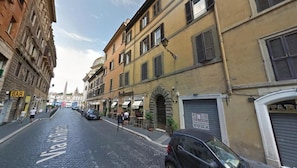 A cobblestone street with buildings on either side, a bar sign, and parked cars.