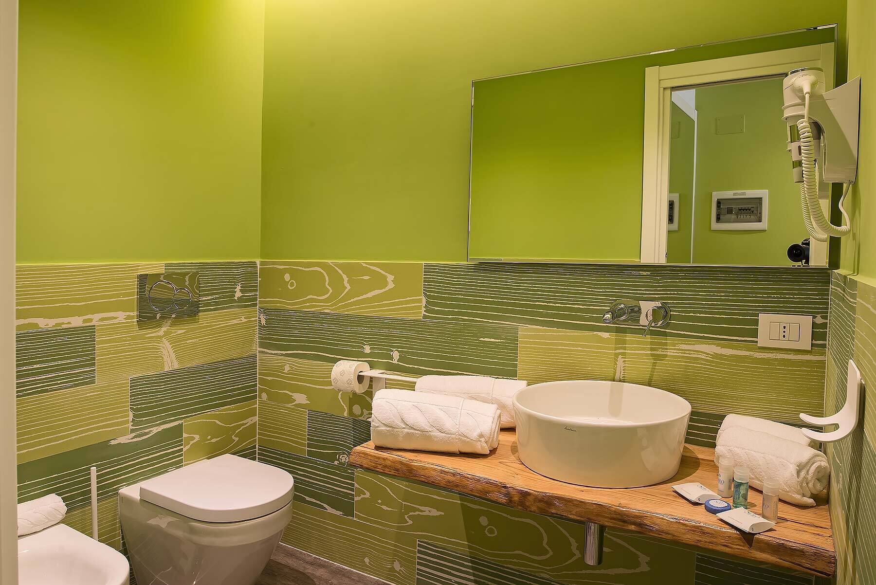 Een badkamer met groene wanden, een wit toilet, een wastafel met spiegel en een handdoekrek.