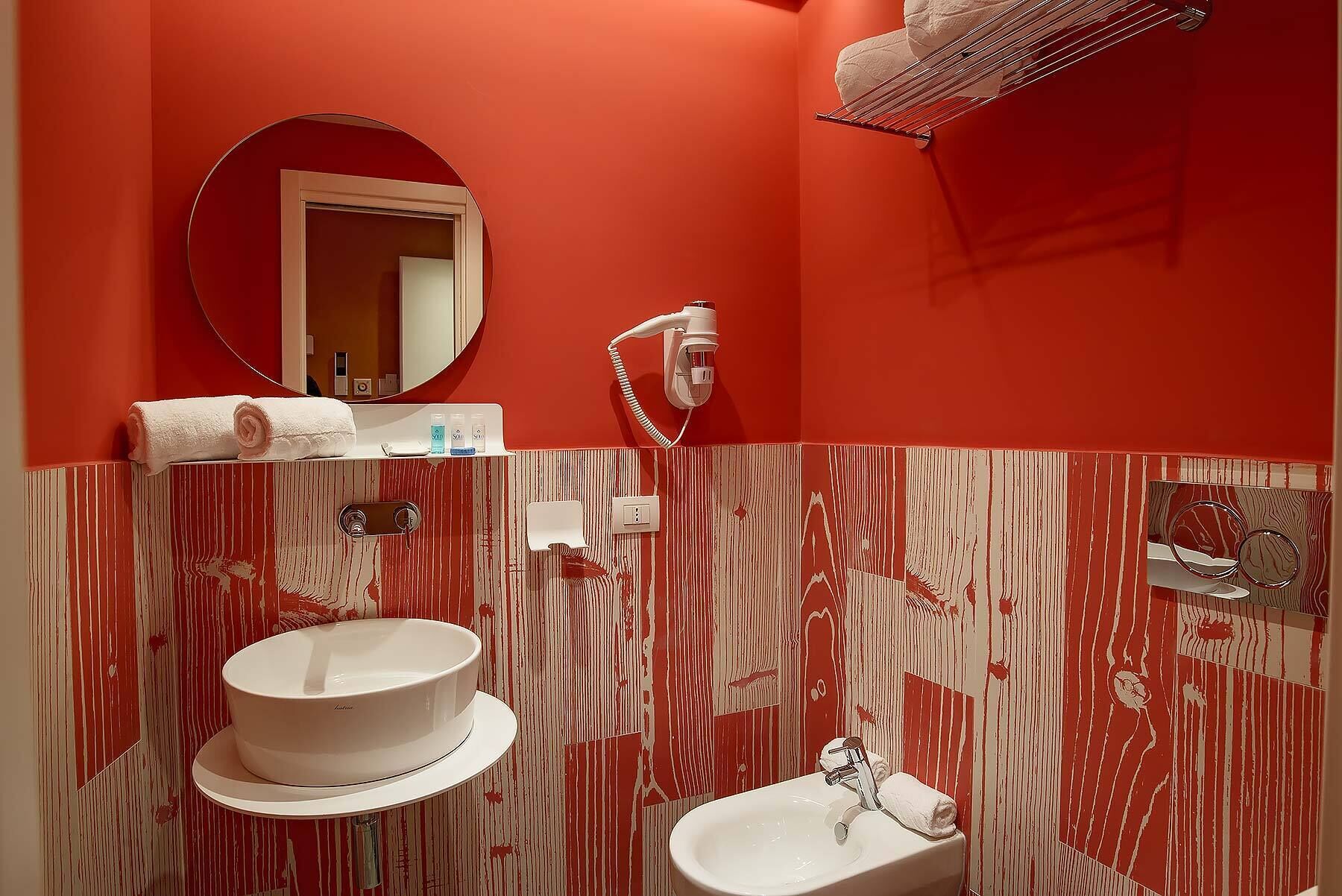 Un baño con espejo redondo, toallero, lavamanos y secador de pelo.