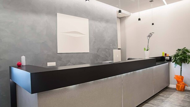 A modern reception desk with a black countertop, a white wall-mounted panel, and a potted plant. - 7 Inn Spanish Steps (Rome)