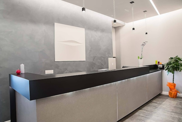 A modern reception desk with a black countertop, a white wall-mounted panel, and a potted plant.