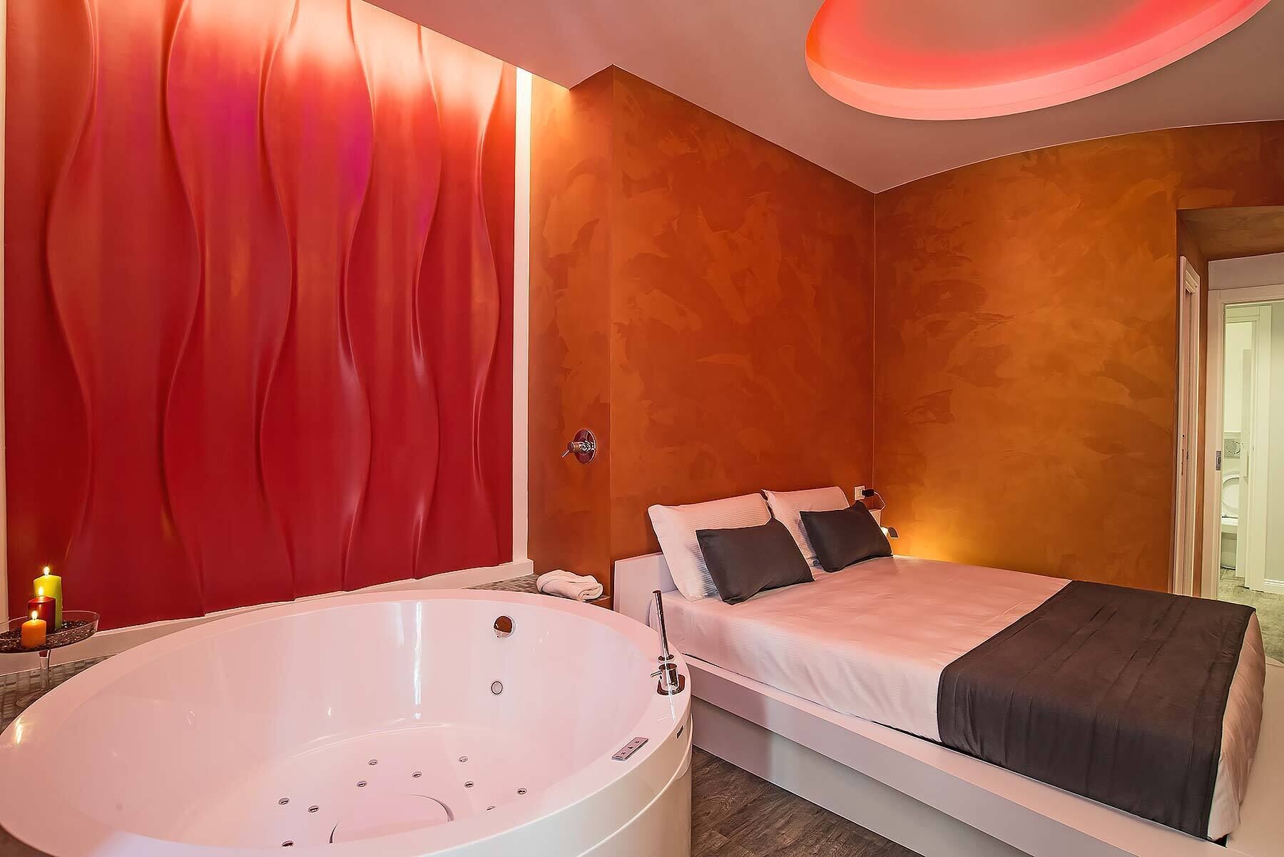 A modern bedroom with a large white bathtub, a bed with two pillows, and a red curtain.