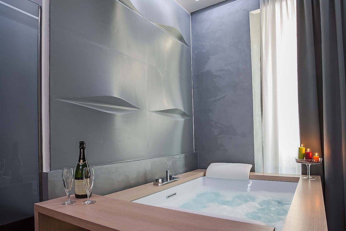 A modern bathroom with a large mirror, a bathtub, and a bottle of champagne on the counter.