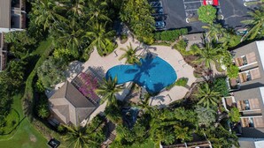 An aerial view of a resort with a swimming pool surrounded by palm trees and a parking lot.