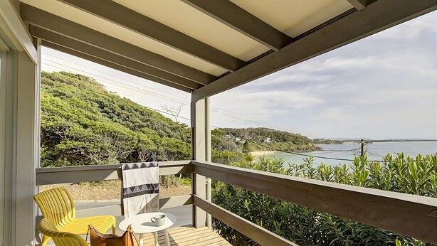 Un balcón con vistas a un paisaje costero, una silla amarilla, una mesa y una toalla a rayas.
