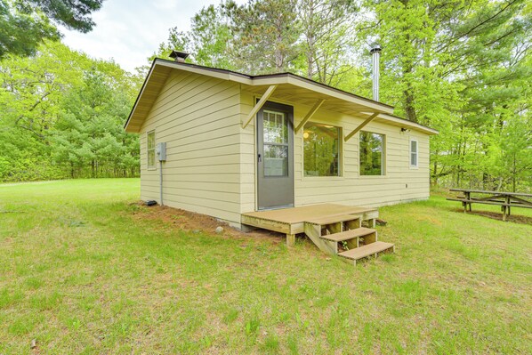 A small, single-story cabin with a front porch and a picnic table in a grassy area surrounded by trees. - Secluded Lakefront Gem on 300 Acres in Webster (Webster)