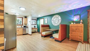 A spacious room with a wooden floor, a dining area with a booth, a refrigerator, and a wall-mounted clock. - Mt Hood Launchpad! Cozy Retro Rhododendron Cabin (Rhododendron)