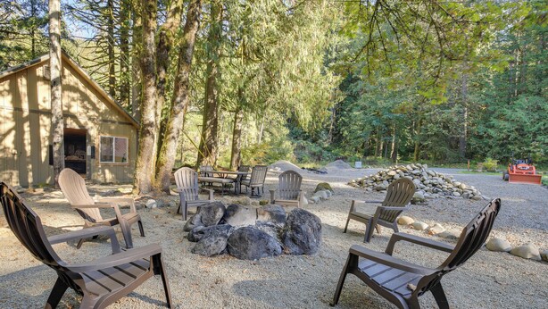 A cabin with a fire pit surrounded by Adirondack chairs, set in a forested area. - Mt Hood Launchpad! Cozy Retro Rhododendron Cabin (Rhododendron)