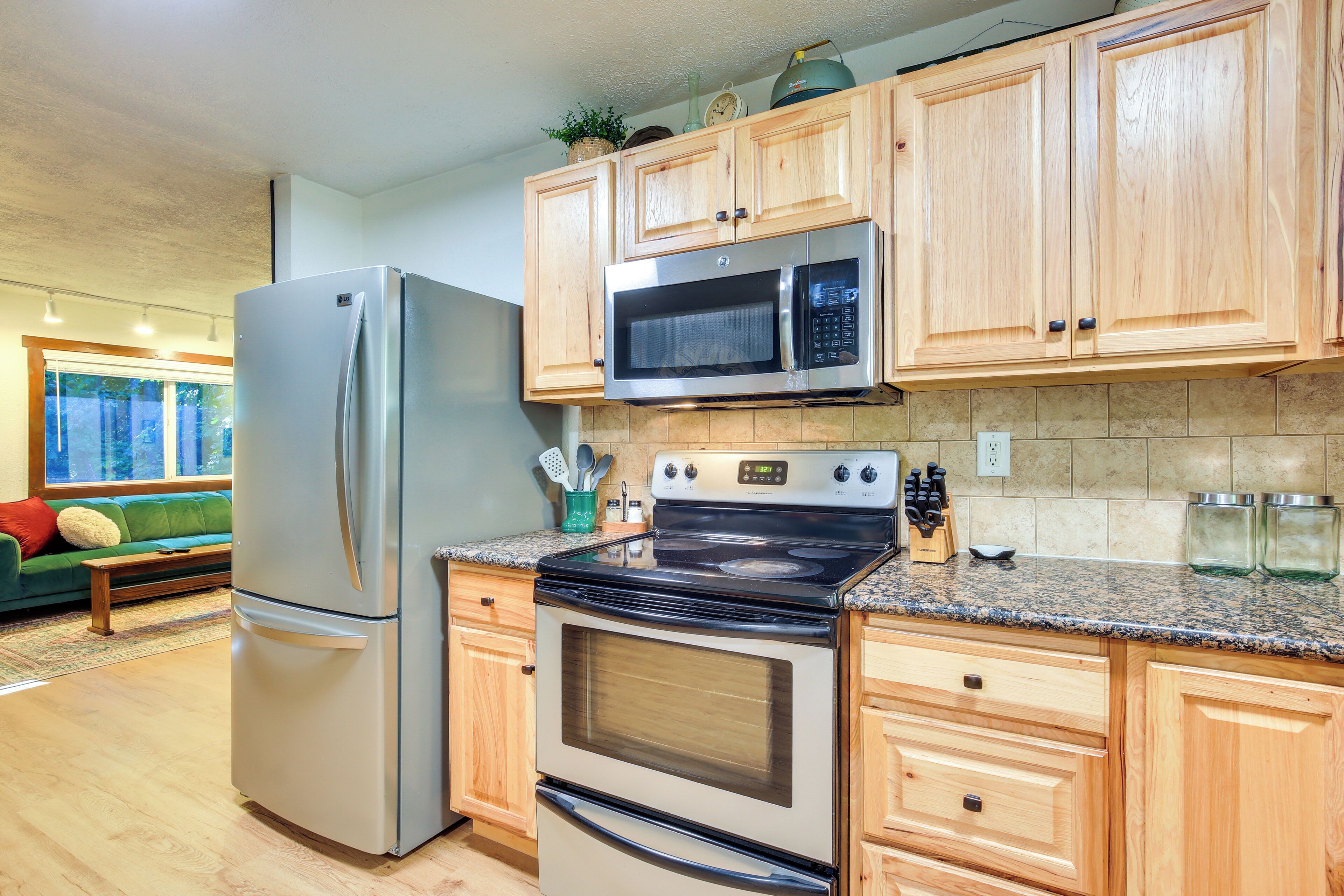 A kitchen with wooden cabinets, a stainless steel refrigerator, a microwave, an oven, and granite countertops.