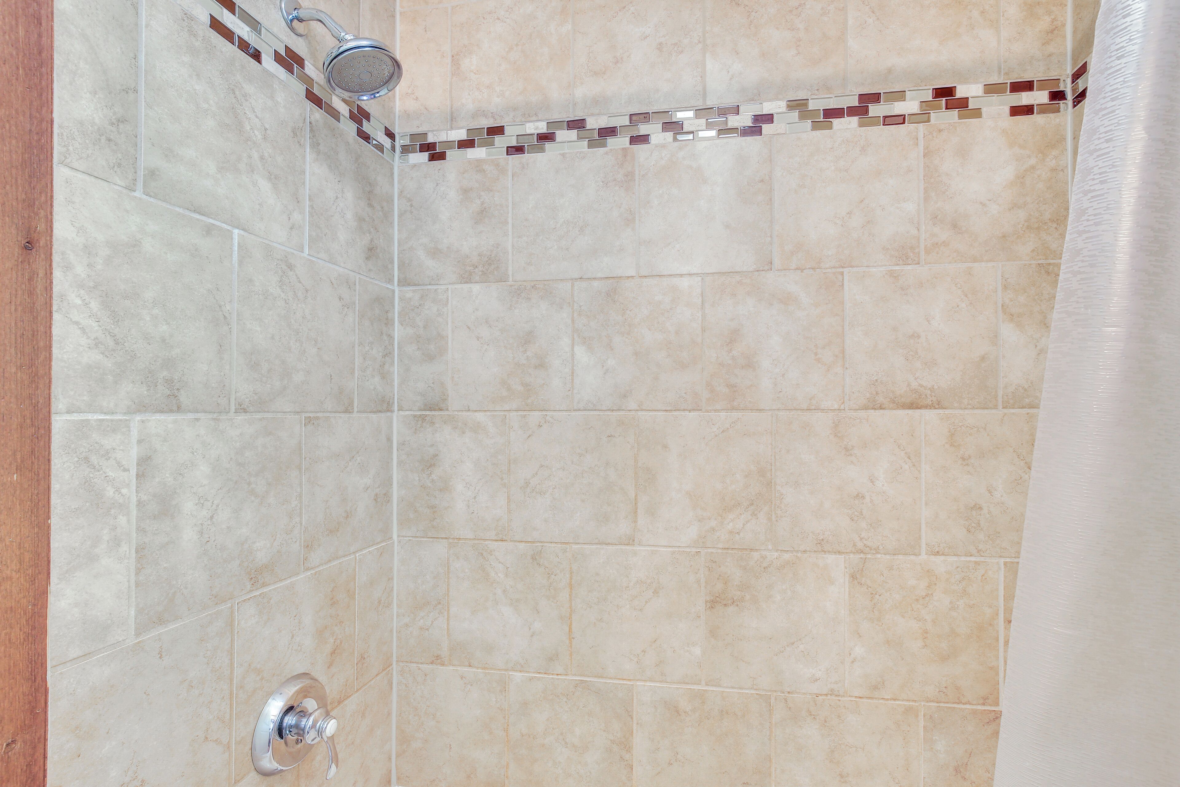 Un área de ducha con azulejos color beige y un borde de mosaico.