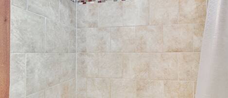 Un área de ducha con azulejos color beige y un borde de mosaico.