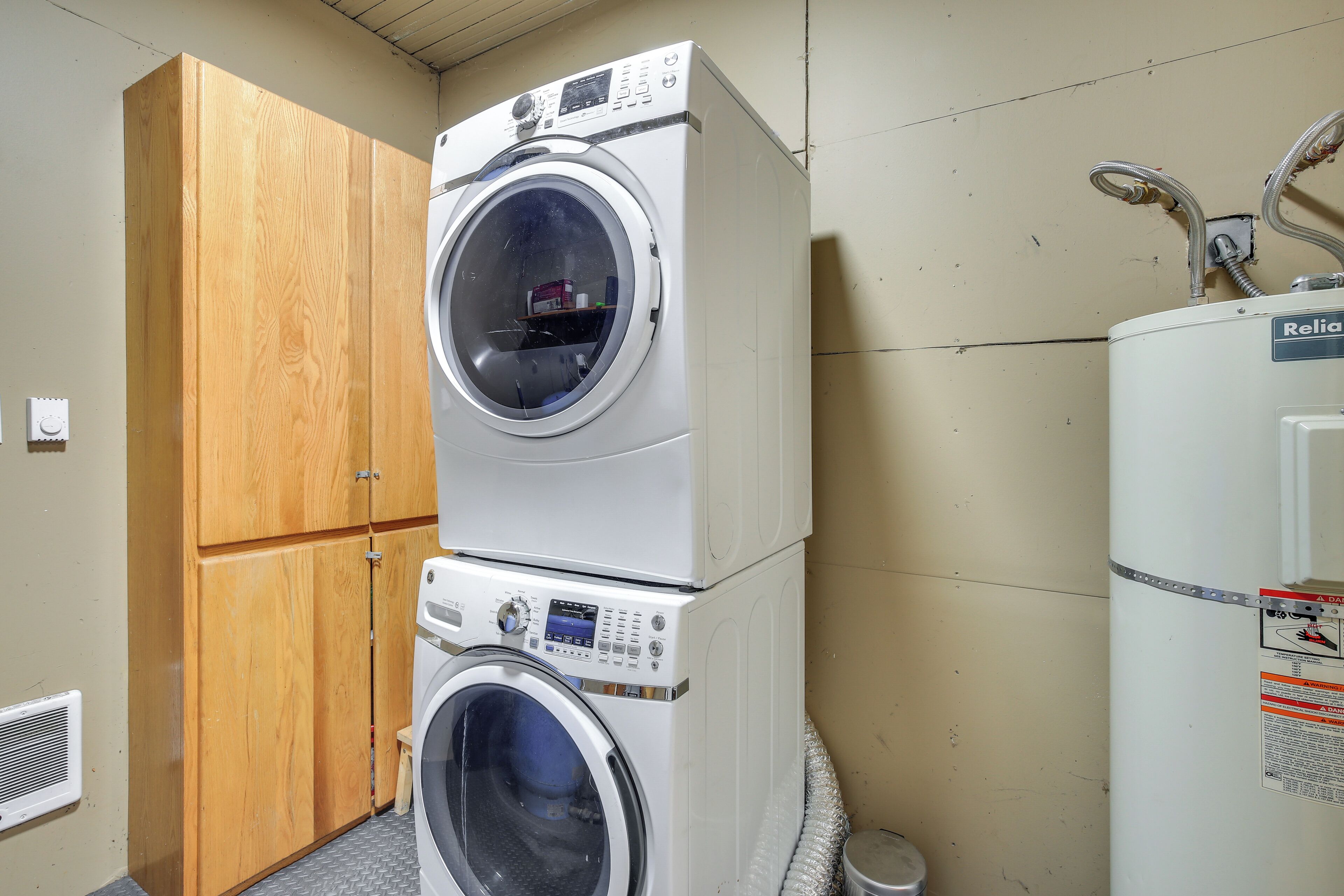 A laundry room with two stacked front-loading washing machines, a wooden cabinet, and a Reliant water heater.