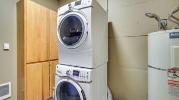 A laundry room with two stacked front-loading washing machines, a wooden cabinet, and a Reliant water heater.