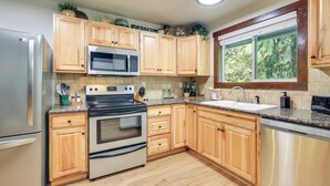 A kitchen with wooden cabinets, stainless steel appliances, a window with a view, and a countertop with various items. - Mt Hood Launchpad! Cozy Retro Rhododendron Cabin (Rhododendron)
