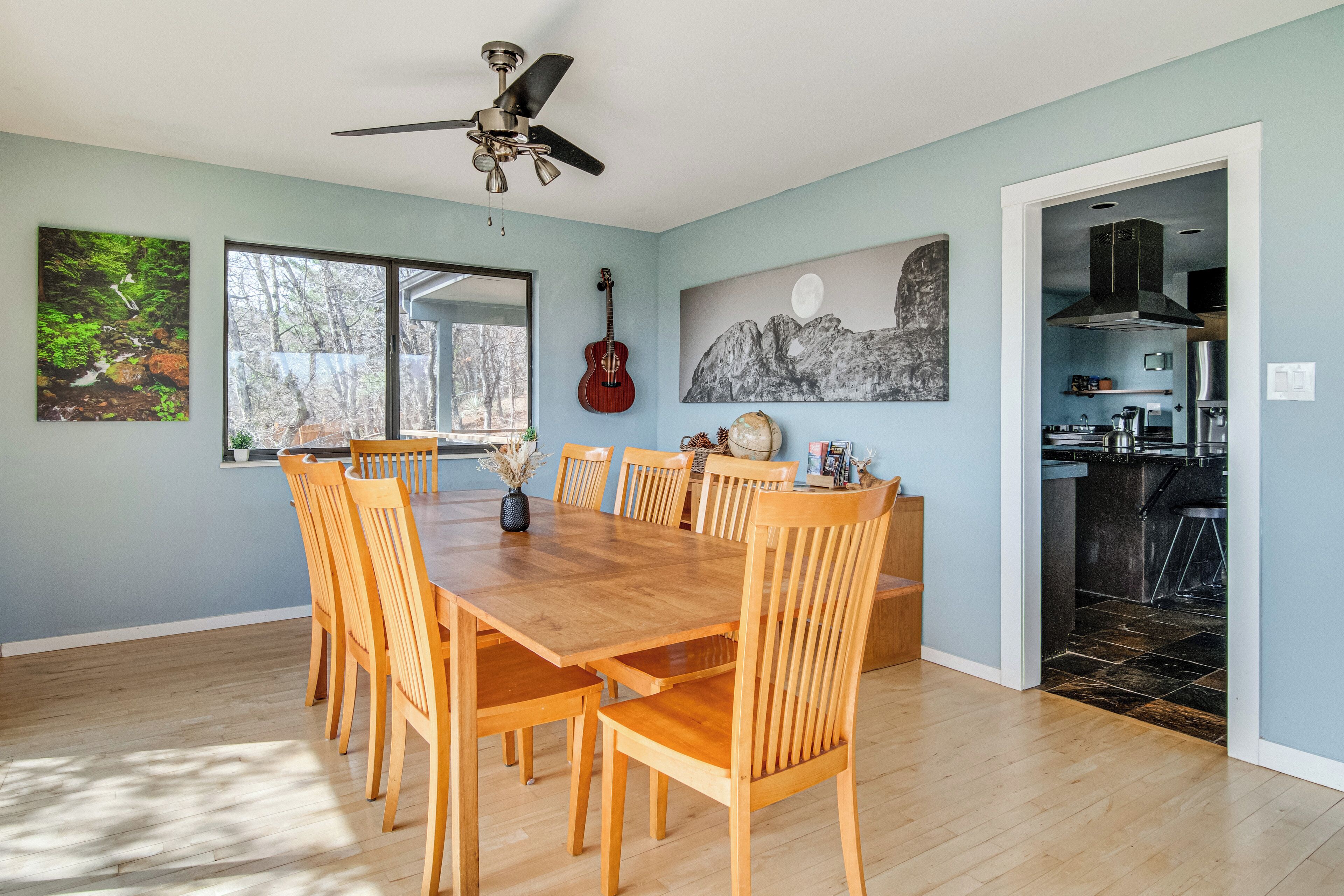 A dining area with a wooden table and chairs, a ceiling fan, and artwork on the walls.