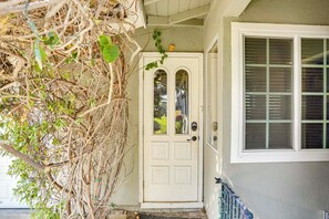 A white door with a glass panel, a window with blinds, and a porch with a railing.