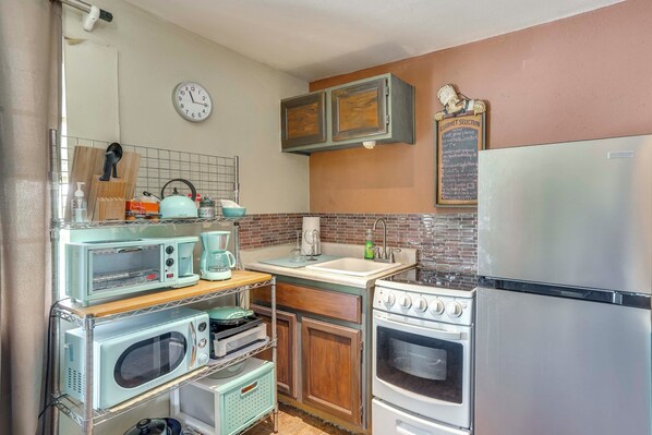 A compact kitchen with a microwave, toaster, coffee maker, sink, and a refrigerator.