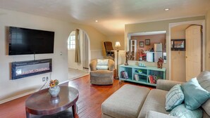 A living room with a flat-screen TV, a fireplace, a sofa, a chair, and a bookshelf. - Pet-friendly Studio in Costa Mesa - 7 Mi to Beach! (Costa Mesa)