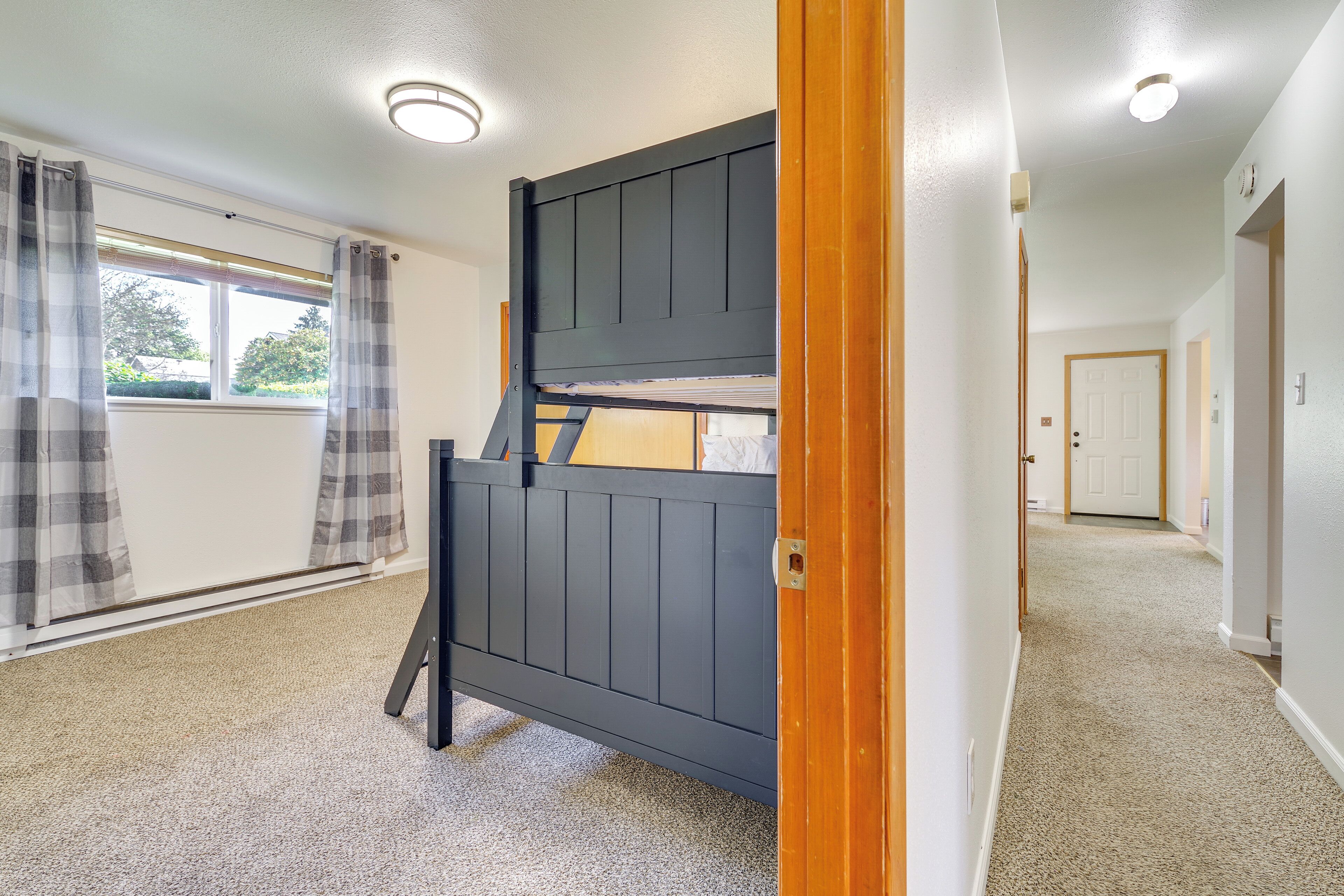 A room with a bunk bed, a window with curtains, and a carpeted floor.
