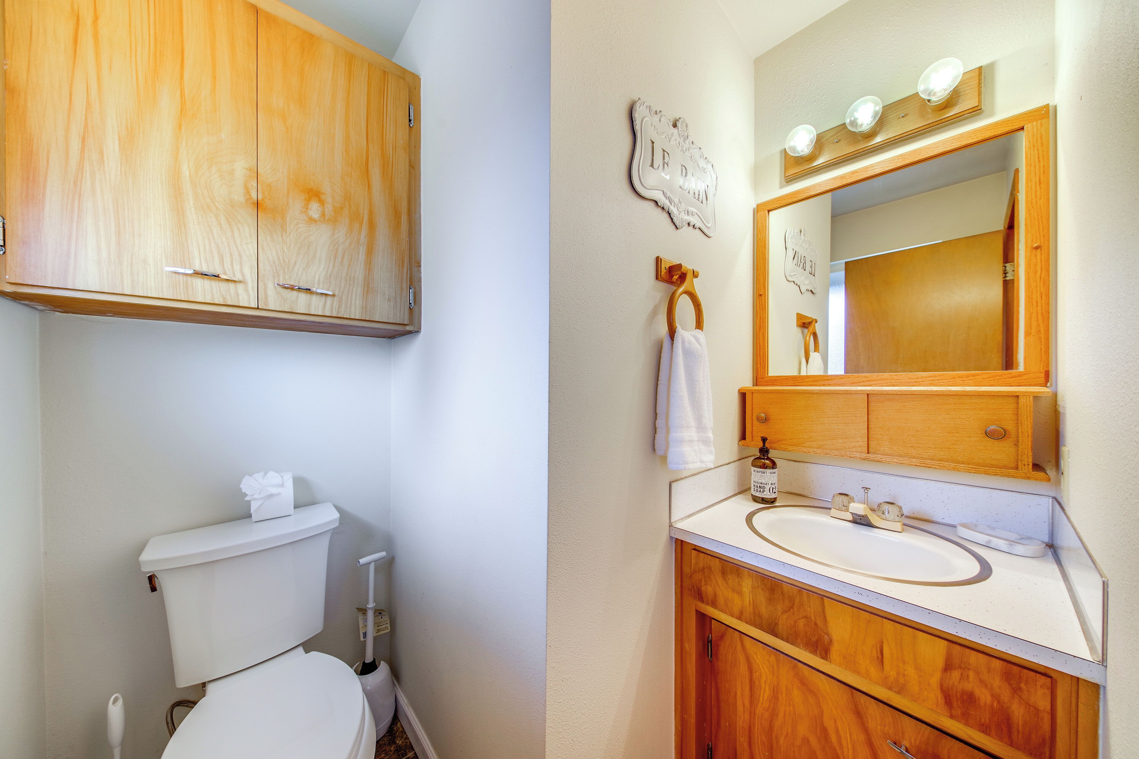 A bathroom with a toilet, wooden cabinets, a sink with a mirror, and a towel hanging on a rack.