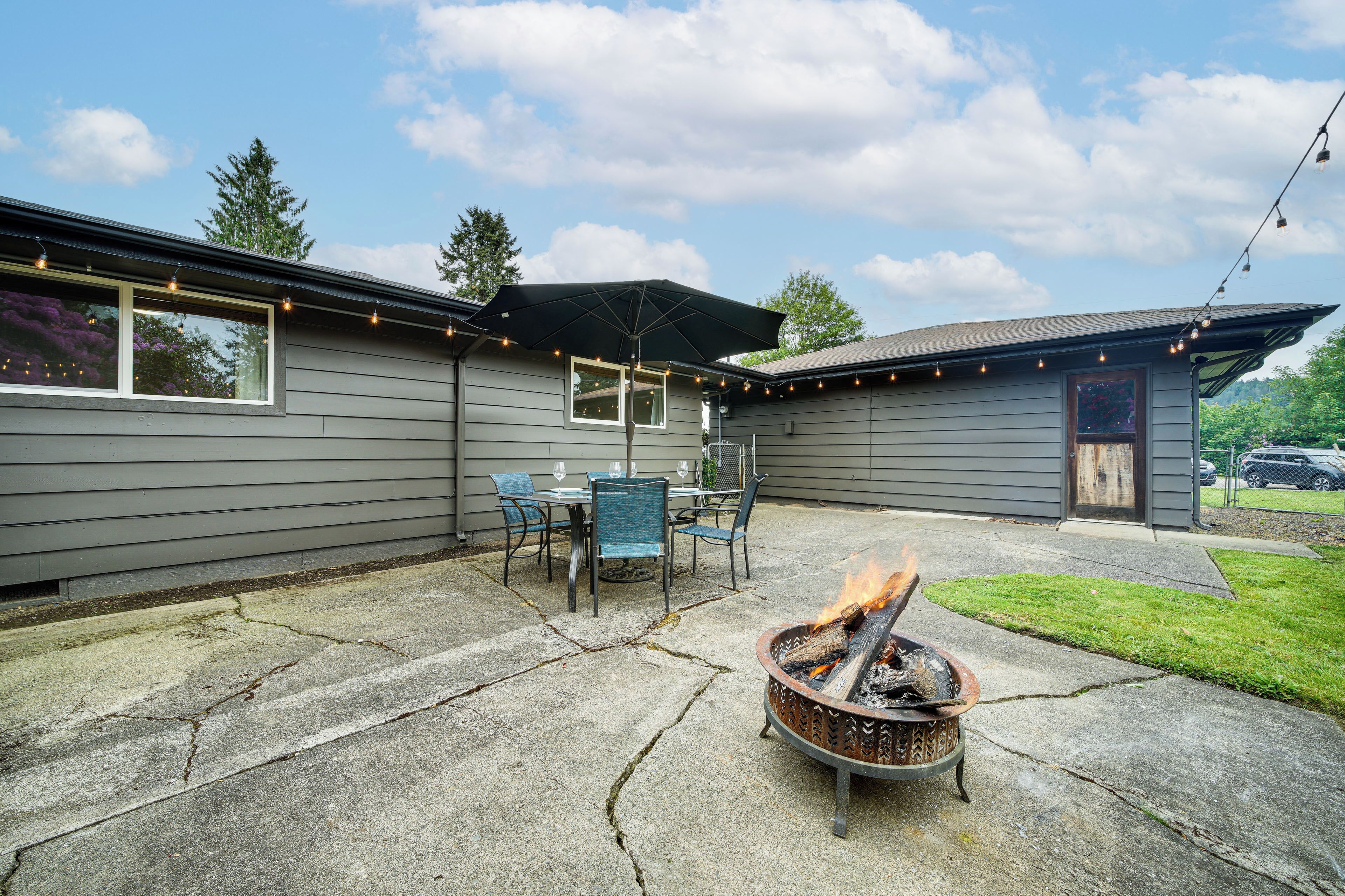 A patio with a fire pit, outdoor furniture, and string lights.