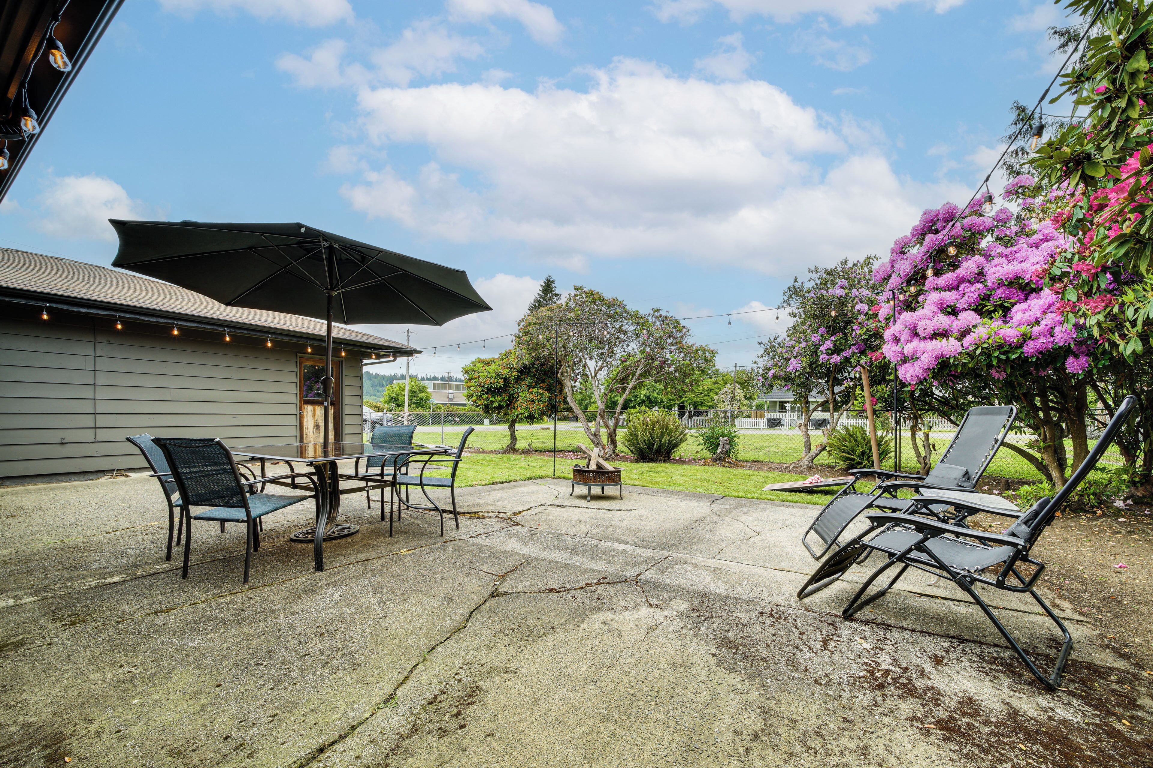 Une terrasse extérieure avec une table et des chaises, un grand parasol et un arbuste fleuri.