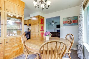 Una mesa de comedor de madera con cuatro sillas, una araña y un cartel en la pared que dice "EAT".
