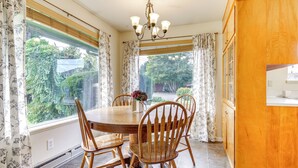 A dining area with a round wooden table, four wooden chairs, a chandelier, and large windows with curtains. - 1 Mi to Snoqualmie River: Pet-friendly Getaway (Carnation)