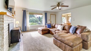 A living room with a sectional sofa, a fireplace, a ceiling fan, and a view of the outdoors. - 1 Mi to Snoqualmie River: Pet-friendly Getaway (Carnation)