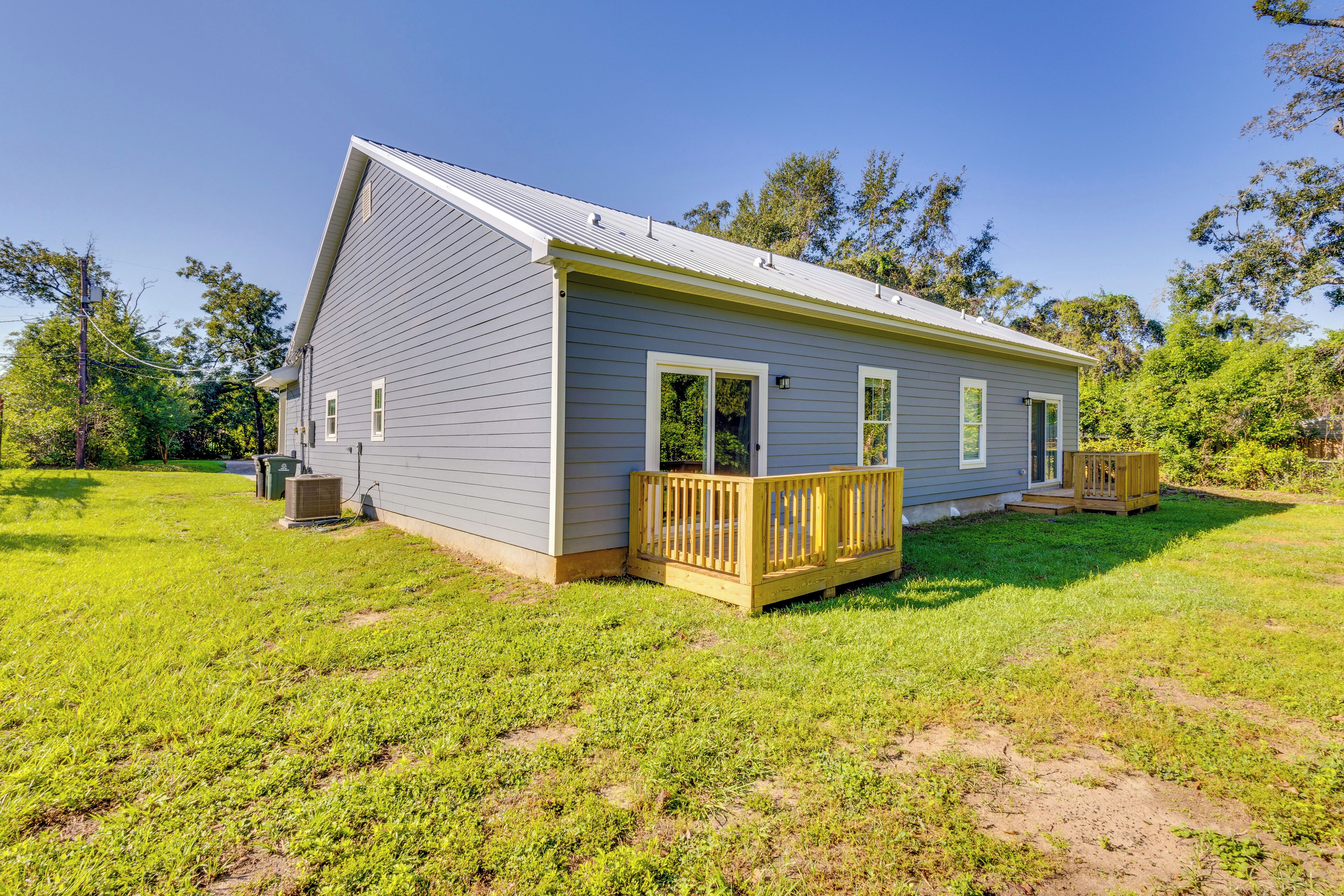 A single-story house with a grey exterior, a wooden deck, and a fenced yard.
