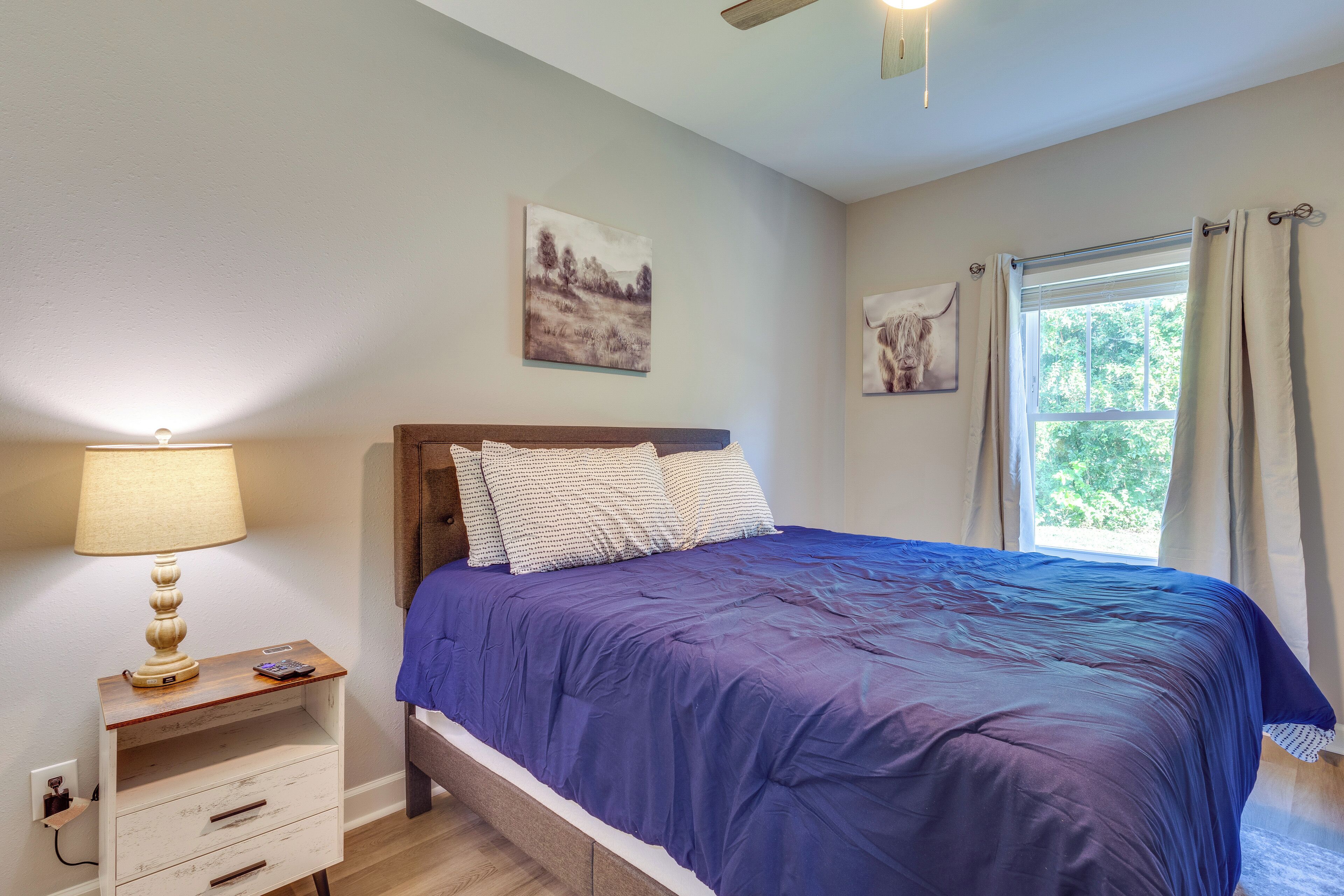 Ein Schlafzimmer mit einem Bett, einem Nachttisch, einer Lampe und zwei an der Wand hängenden Bildern.