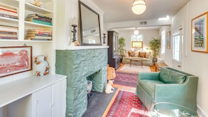 A living room with a fireplace, a green sofa, and a bookshelf filled with books. - Cottage w/ Furnished Patio & Garden: Dtwn Leesburg (Leesburg)