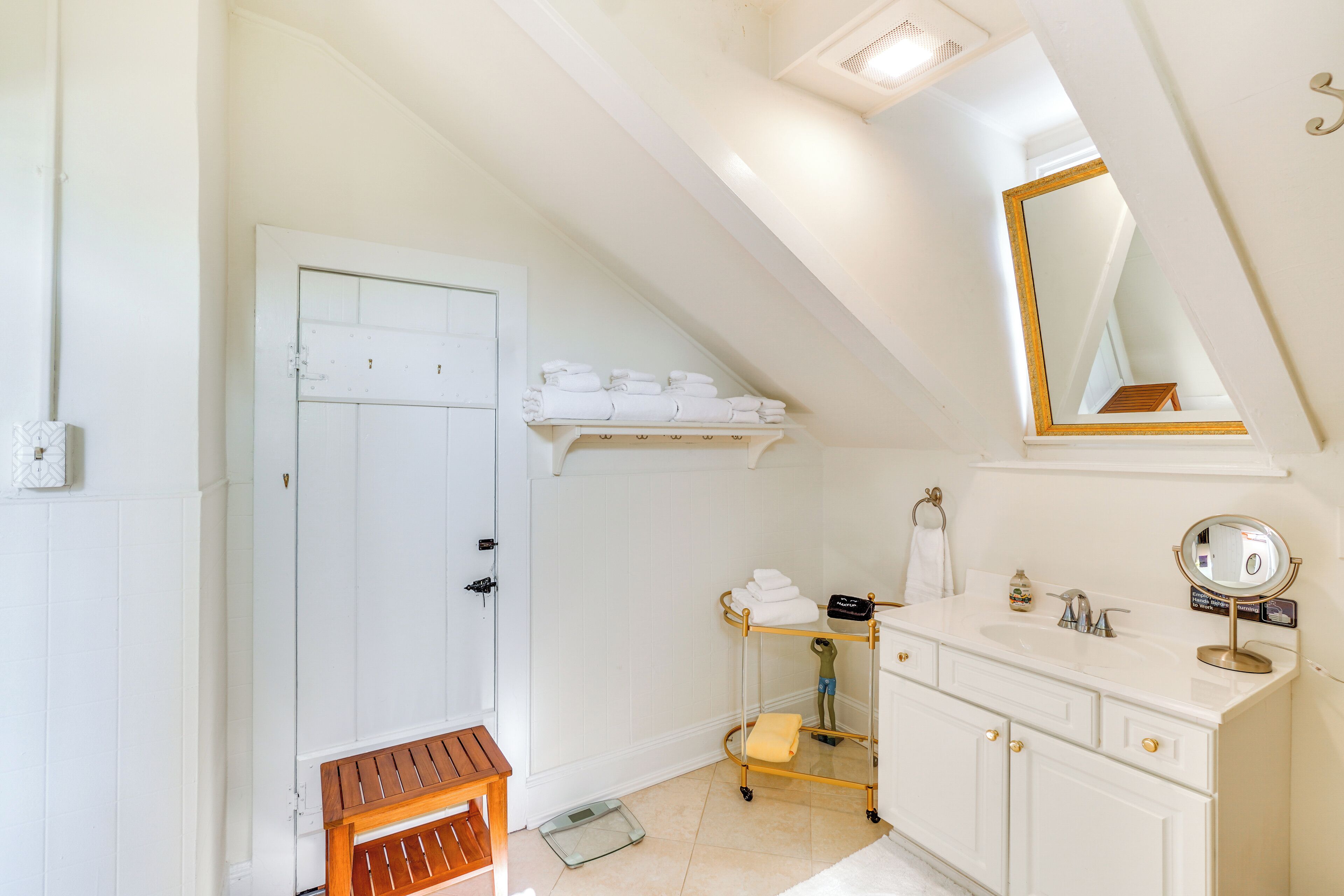 A bathroom with a white vanity, a mirror, a towel rack, and a bench.