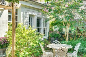 Un jardín con una pérgola de madera, una mesa con sillas y diversas plantas y flores.