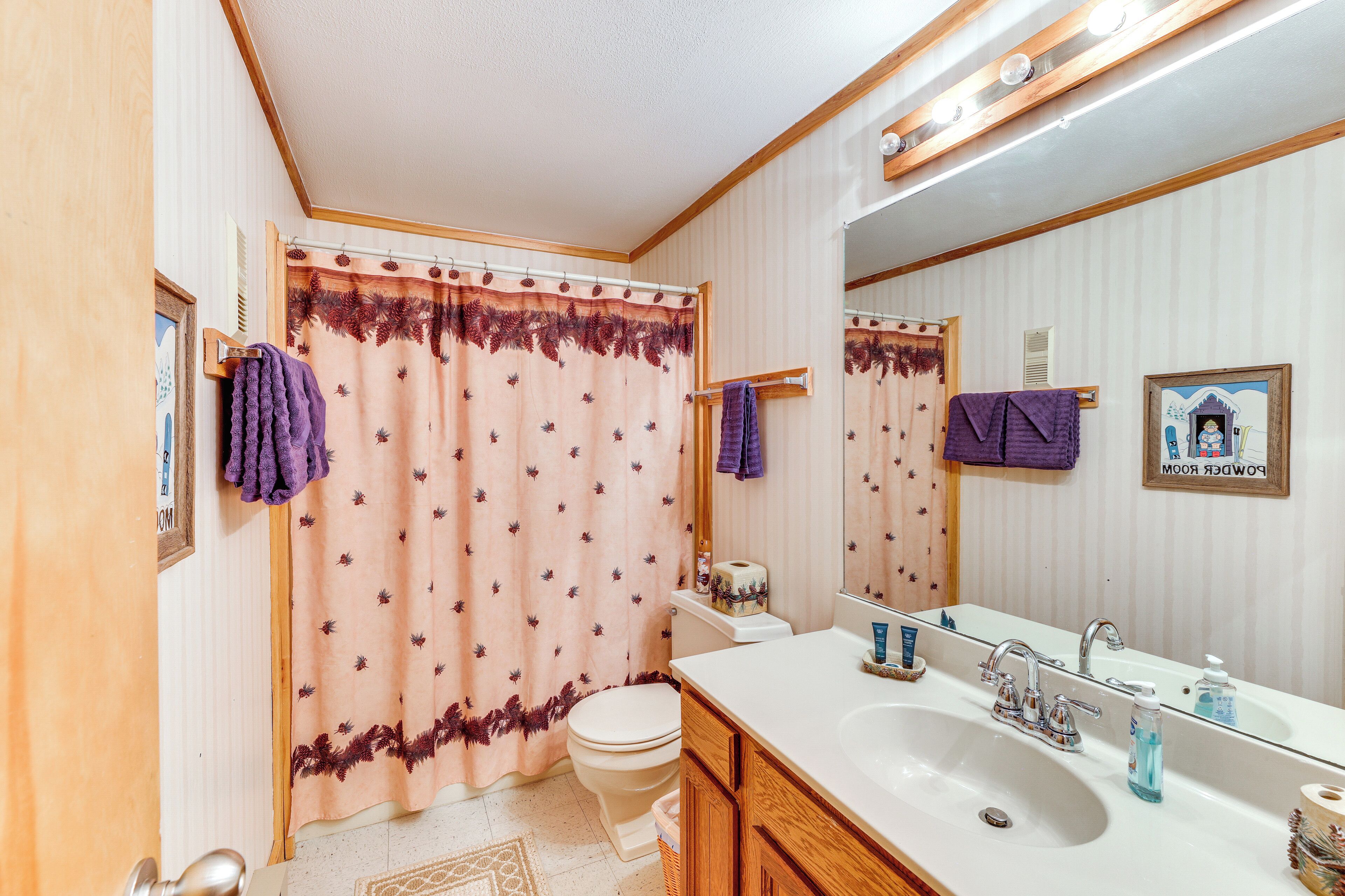 A bathroom with a shower curtain, toilet, sink, and mirror.