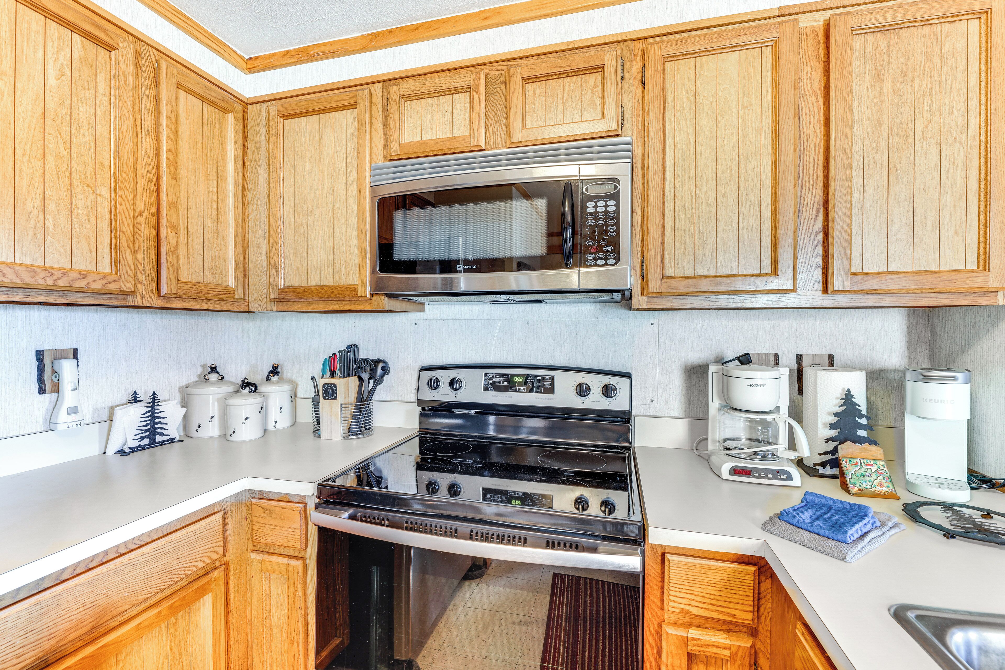 A kitchen with wooden cabinets, a stainless steel microwave, a stove, and a coffee maker.