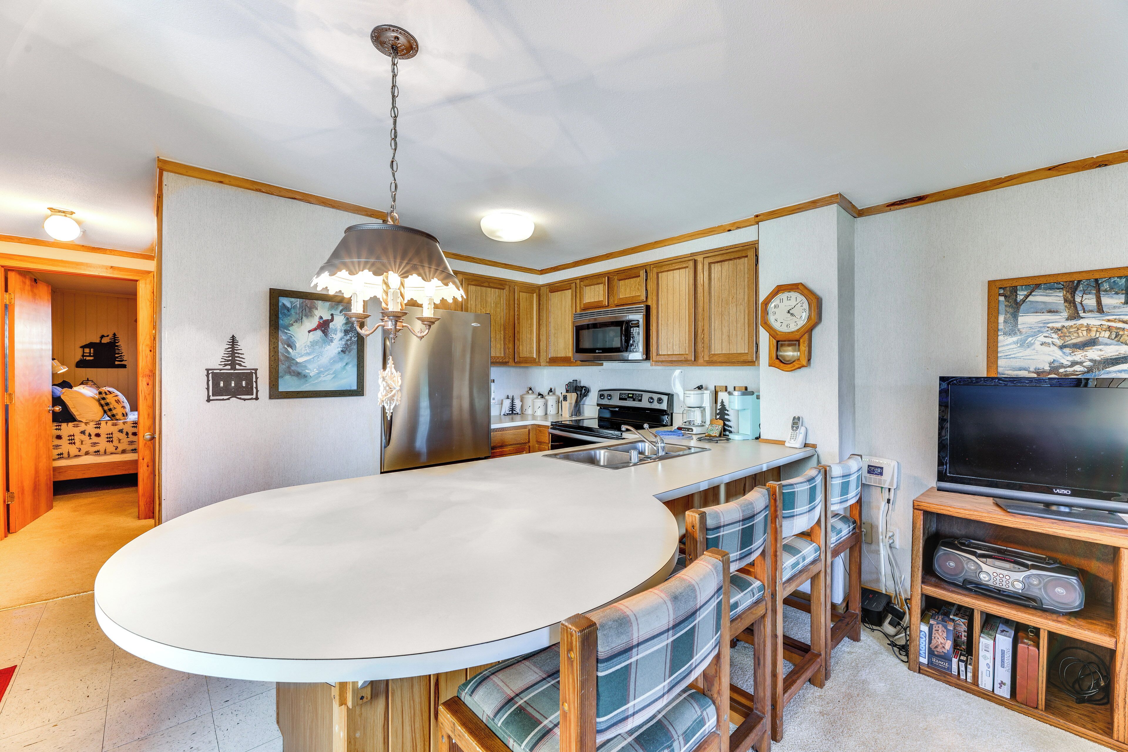A modern kitchen with wooden cabinets, a central island, a built-in microwave, and a large flat-screen TV.