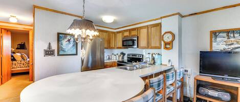 A modern kitchen with wooden cabinets, a central island, a built-in microwave, and a large flat-screen TV.