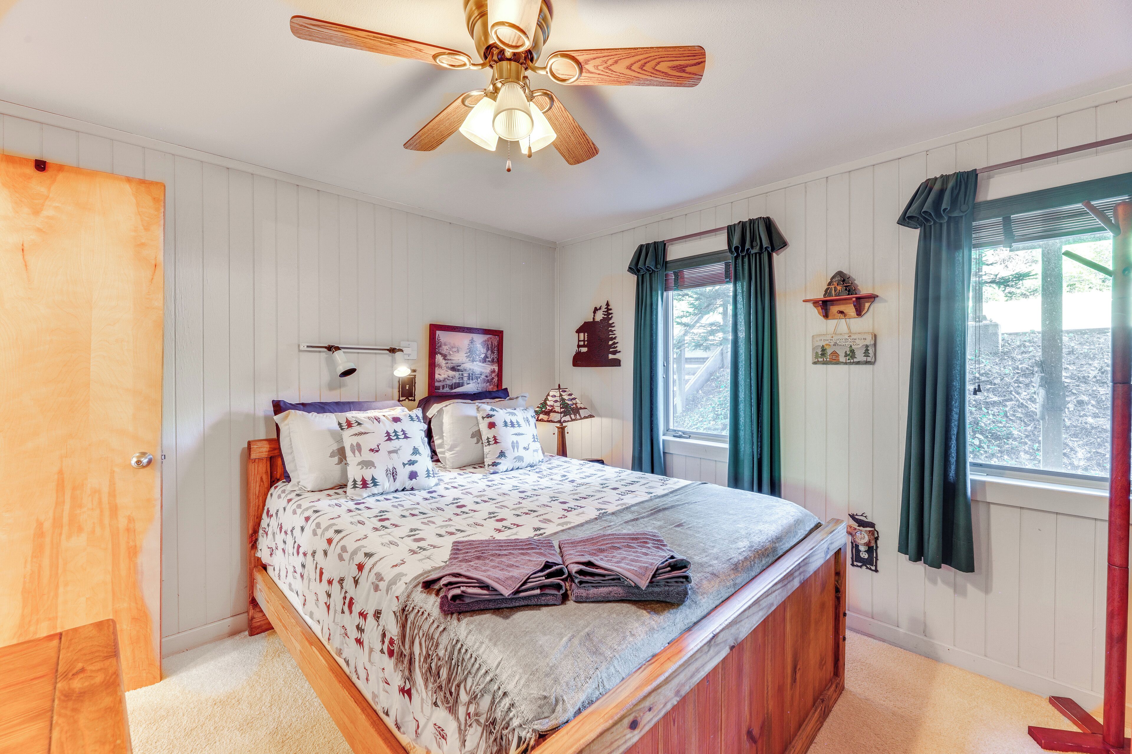 A bedroom with a wooden bed, a ceiling fan, a window with curtains, and a wall-mounted shelf with a clock.